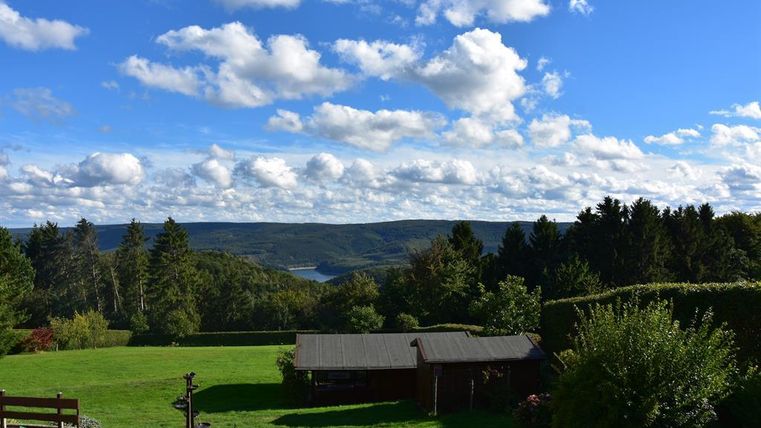 Eine malerische Landschaft mit sanften Hügeln und einem klaren blauen Himmel. Im Vordergrund befindet sich eine grüne Wiese mit einem Brunnen.