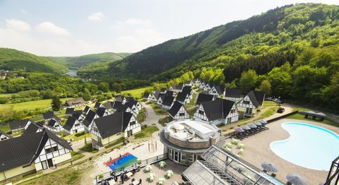 Eine malerische Ferienanlage inmitten von grünen Hügeln. Zu sehen sind gemütliche Häuser und ein Poolbereich mit Liegen.