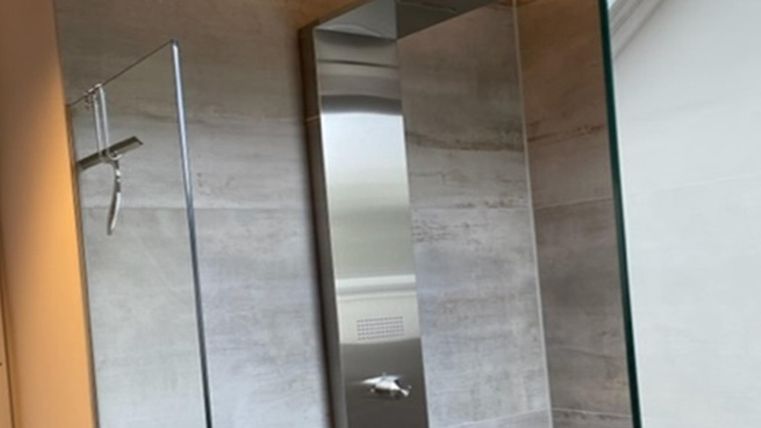 Eine moderne Dusche mit gläserner Trennwand und Edelstahlarmaturen. Die Wände sind mit einem schlichten, grauen Material bedeckt.