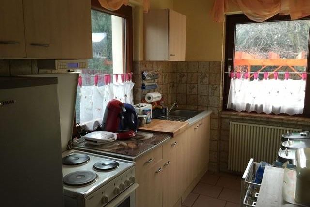 Eine gemütliche Küche mit modernen Geräten und einem hellen Fenster. Die Fenster sind mit freundlichen Vorhängen geschmückt, und es gibt Geschirr auf der Arbeitsplatte.