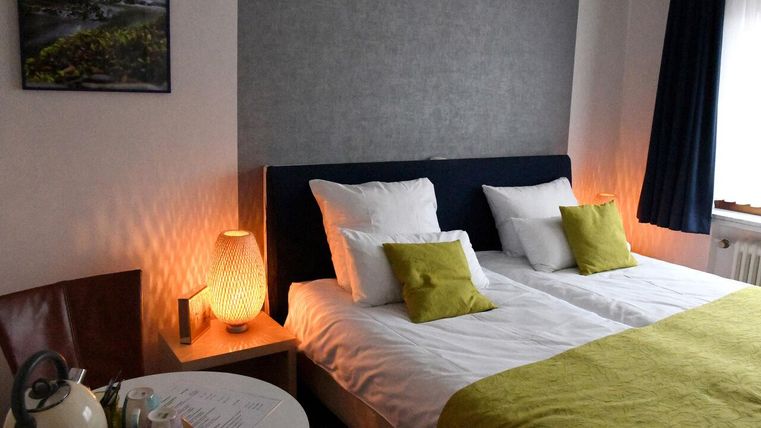 Ein gemütliches Schlafzimmer mit zwei Einzelbetten und hellen Kissen. Neben dem Bett steht ein kleiner Tisch mit einem Wasserkocher und Teetassen.