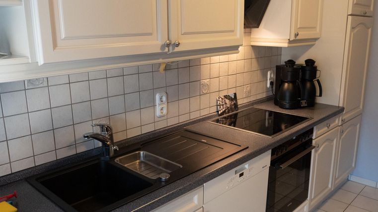 Eine moderne Küche mit hellen Schränken und einer Arbeitsplatte aus dunklem Material. Der Raum ist gut beleuchtet und enthält Kochgeräte sowie ein Spülbecken.