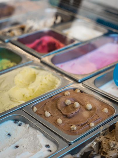 Eine Auswahl an verschiedenen Eissorten in Metalldosen. Die Farben reichen von hellgelb über rosa bis zu schokoladigen Brauntönen.