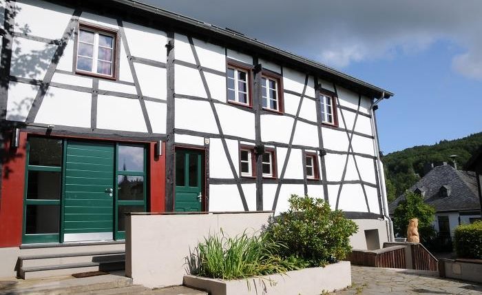 Ein modernes Fachwerkhaus mit grünen Türen und Fenstern. Der Eingangsbereich ist von einer gepflegten Gartenlandschaft umgeben.