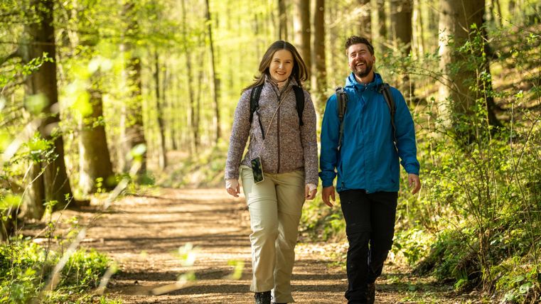 Ein Paar wandert auf einem Waldweg und genießt die Natur. Umgeben von grünen Bäumen strahlen sie Freude und Entspannung aus.