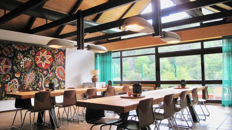 Ein moderner Raum mit einem langen Tisch und stilvollen Stühlen. Große Fenster fluten den Raum mit natürlichem Licht und bieten einen Blick ins Grüne.