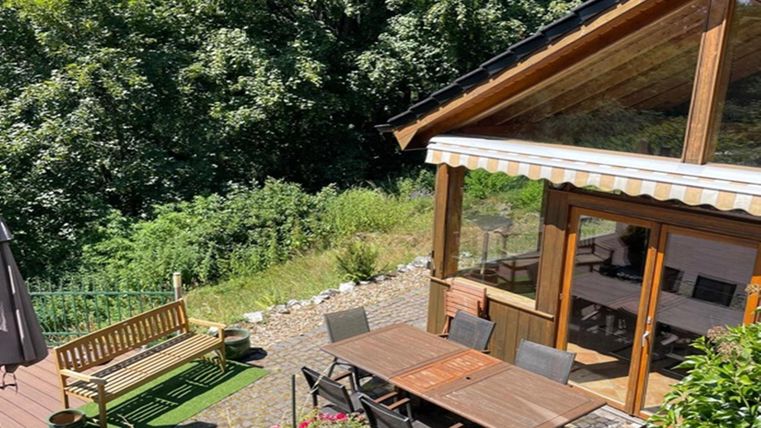 Ein gemütliches Holzhaus mit einer Terrasse und einem Esstisch im Freien. Die Umgebung ist grün und einladend, ideal für entspannte Stunden.