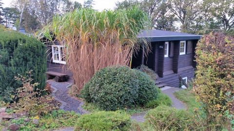 Ein hübsches Haus mit dunkler Fassade, umgeben von üppigen Pflanzen und Büschen. Der Garten ist liebevoll gestaltet und schafft eine angenehme Atmosphäre.