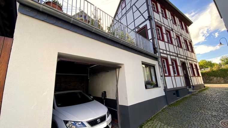 Ein modernes Haus mit Fachwerkarchitektur und einem Garagenbereich. In der Garage steht ein weißes Auto.