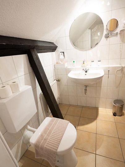 Ein kleines Badezimmer mit einem Waschbecken, einem Spiegel und einer Toilette. Die Wände sind mit weißen Fliesen gefliest, und der Boden ist fliesenähnlich.