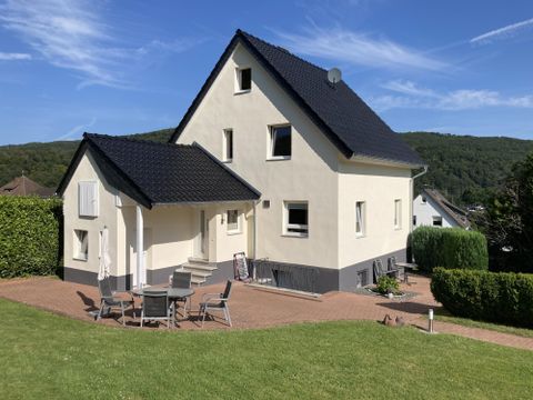 Ein modernes, helles Haus mit einem schwarzen Dach und einer einladenden Terrasse. Der Garten ist gepflegt und die Landschaft ist grün.
