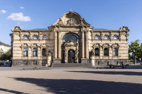 Eine Hand hält ein gebogenes Blatt Papier. Der Hintergrund enthält Informationen über eine Ausstellung im Leopold-Hoesch-Museum.