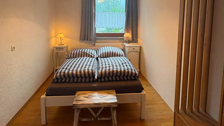 Ein gemütliches Schlafzimmer mit einem Doppelbett und karierten Bettdecken. Die warmen Holztöne und Fenster sorgen für eine einladende Atmosphäre.
