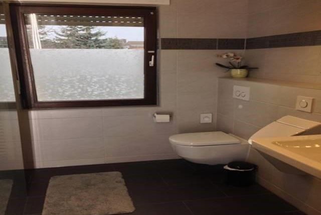 Ein modernes Badezimmer mit einer Toilette und einem Waschbecken. Das Fenster lässt viel Tageslicht herein und bietet einen Blick auf die Natur.
