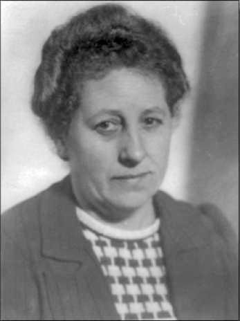 Das Bild zeigt eine Frau mit lockigem Haar und einem neutralen Gesichtsausdruck. Sie trägt einen gestreiften Pullover und eine Jacke.