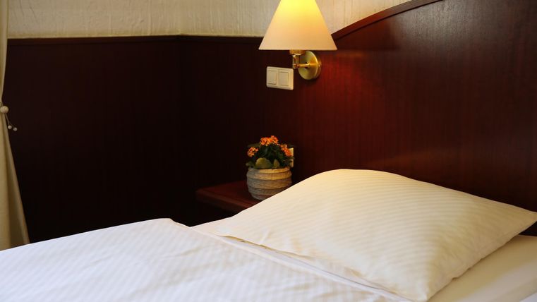 Ein gemütliches Schlafzimmer mit einem großen Bett und einem Nachttisch. Eine Nachttischlampe und eine kleine Pflanze sorgen für eine einladende Atmosphäre.