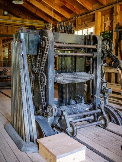 Eine alte Druckmaschine steht in einem Holzgebäude. Sie zeigt die Mechanik und das handwerkliche Design vergangener Zeiten.