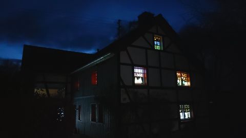 Ein altes Fachwerkhaus im Dunkeln mit bunten Fenstern. Der Himmel ist dunkelblau, was eine gemütliche Atmosphäre schafft.