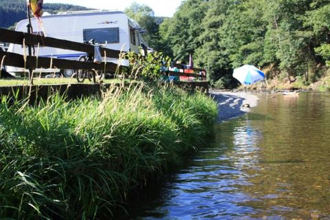 Ein Campingplatz in einer grünen Umgebung mit vielen Bäumen. Verschiedene Wohnmobile und Zelte sind sichtbar zwischen der Natur.
