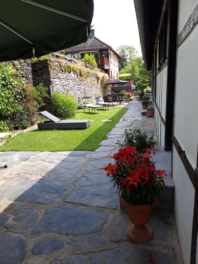 Ein schöner Garten mit gepflegtem Rasen und blühenden roten Blumen. Im Hintergrund sind gemütliche Sitzgelegenheiten und ein modernes Haus zu sehen.