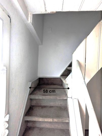 Eine Treppe mit Teppichboden führt nach oben. Die Breite der Treppe beträgt 58 cm.