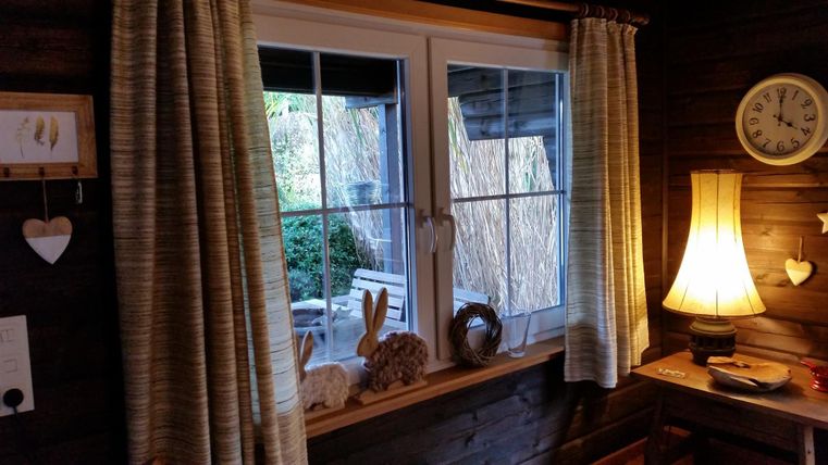 Ein gemütlicher Raum mit einem Fenster, durch das man einen Garten sehen kann. Neben dem Fenster steht eine Lampe und es sind weitere dekorative Elemente sichtbar.