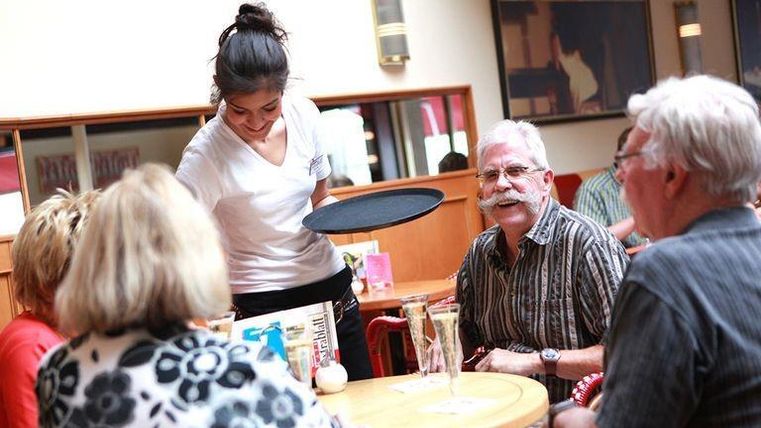 Eine Kellnerin bedient einen Tisch mit mehreren Gästen in einem Restaurant. Die Atmosphäre ist freundlich und einladend.