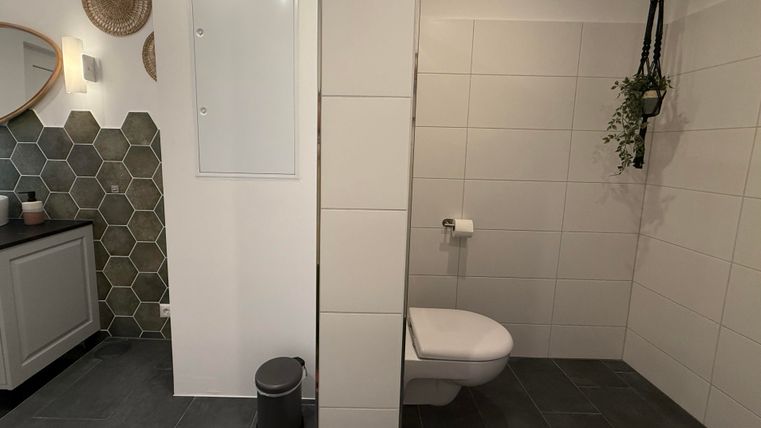 Ein modernes Badezimmer mit hexagonalen Fliesen und einem eleganten Waschbecken. Die Wände sind hell gefliest, und eine grüne Pflanze hängt dekorativ.