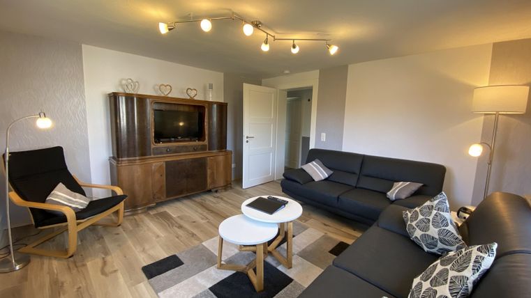 Ein modernes Wohnzimmer mit einem gemütlichen Sofa, einem Fernseher und einem stilvollen Tisch. Das Raumdesign ist hell und einladend, mit Holzfußboden und angenehmer Beleuchtung.