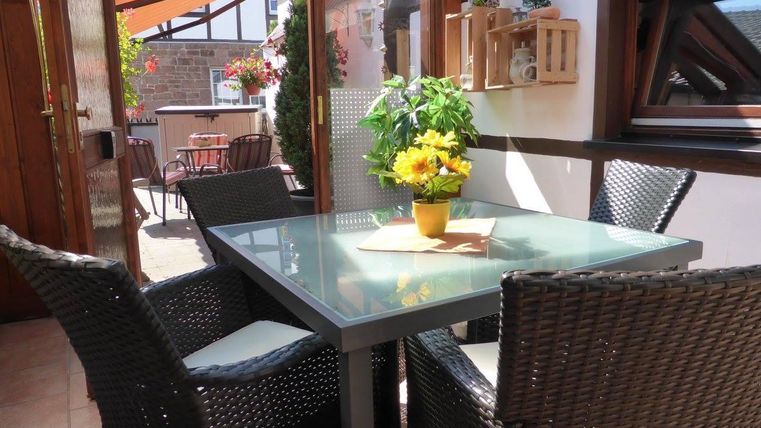 Ein gemütlicher Innenhof mit einem gläsernen Tisch und schönen Stühlen. Auf dem Tisch steht ein blühender Topf mit sonnigen Blumen.