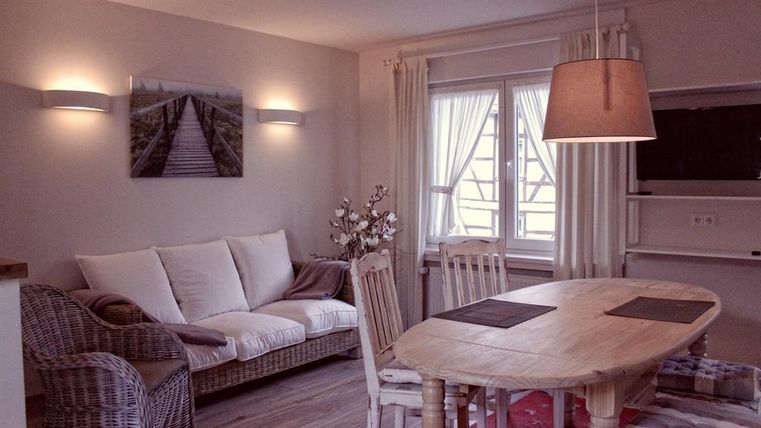 Ein gemütlicher Wohn- und Essbereich mit einem runden Holztisch und Stühlen. Der Raum ist hell und freundlich, mit einem Sofa und natürlichem Licht durch große Fenster.
