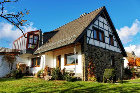 Ein gemütliches Haus mit einer Mischung aus modernen und traditionellen Elementen. Es ist von einem gepflegten Garten umgeben und hat einen klaren blauen Himmel im Hintergrund.