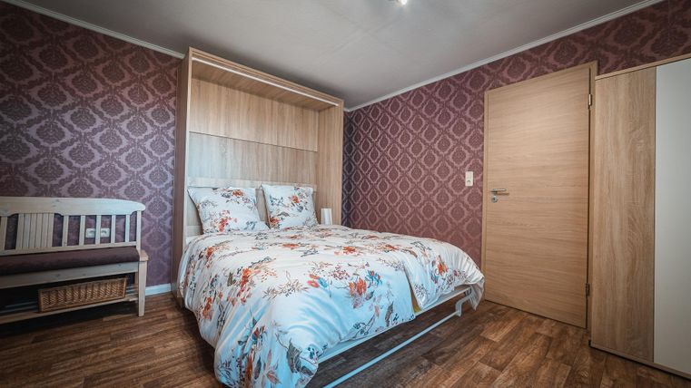 Ein gemütliches Schlafzimmer mit einem Doppelbett und einer Holzverkleidung. Die Wände sind mit einem eleganten Muster dekoriert, und ein Gitterbett ist ebenfalls im Raum vorhanden.