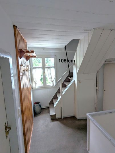 Ein heller Flur mit einer Treppe und einem angrenzenden Raum. Die Höhe der Treppe beträgt 105 cm.