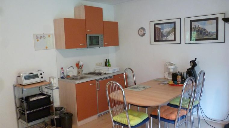 Eine moderne Küche mit Holzschränken und hellen Wänden. Der Essbereich hat einen ovalen Tisch mit bunten Stühlen und verschiedenen Küchengeräten.