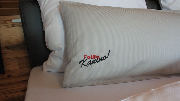 Ein Kissen mit dem Aufdruck „Frau Kanuro!“ liegt auf einem Bett. Der Hintergrund zeigt eine natürliche Holzoptik.