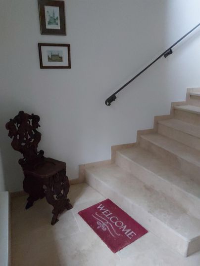 Ein einladender Eingangsbereich mit einer Treppe und einem Holzstuhl. Auf dem Boden liegt eine Willkommensmatte.