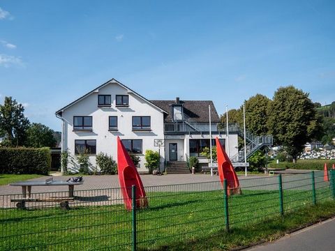 Ein modernes Gebäude mit weißen Wänden und einer großen Terrasse. Vor dem Haus stehen rote Boote und eine gepflegte Grünfläche.
