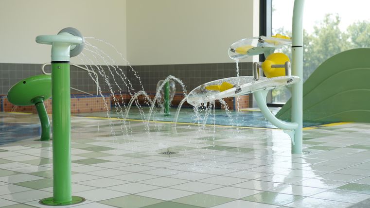 Ein Spritzbereich mit bunten Wasseranlagen. Die Fliesen sind hell und sauber, ideal für Kinder.