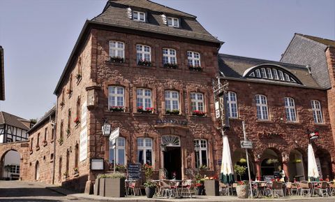 Ein traditionelles Gebäude mit roter Steinfassade und vielen Fenstern. Vor dem Haus stehen Tische und Stühle, die zum Verweilen einladen.