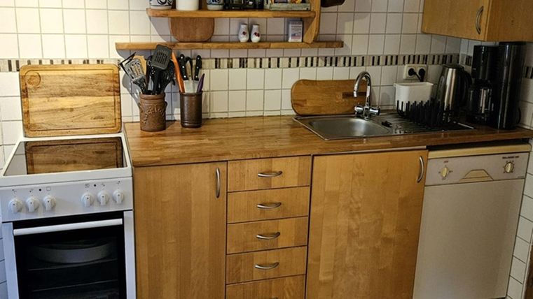 Eine moderne Küche mit Holzoberflächen und weißen Fliesen. Es gibt einen Herd, eine Spüle und eine Geschirrspülmaschine.