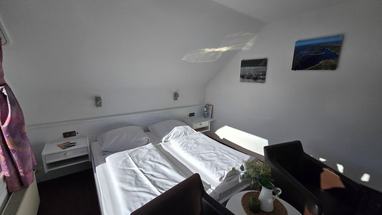 Ein gemütliches Schlafzimmer mit zwei Betten und einem kleinen Tisch. Die Wände sind mit Bildern dekoriert und es gibt viel natürliches Licht.