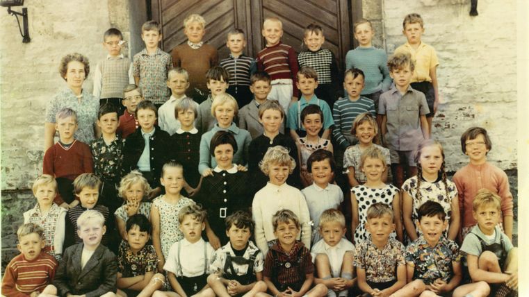 Eine Gruppe von Kindern steht vor einer großen Tür. Sie sind in verschiedenen Kleidungsstilen gekleidet und lächeln zur Kamera.
