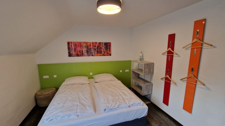 Ein modernes Schlafzimmer mit einem Doppelbett und bunten Wänden. Es gibt praktische Ablageflächen und Dekorationselemente.