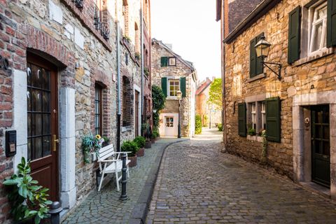 Eine charmante Gasse mit kopfsteingepflastertem Boden und historischen Steinhäusern. Grüne Fensterläden und Pflanzen verleihen der Szenerie eine einladende Atmosphäre.