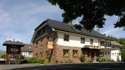 Ein traditionelles Gasthaus mit einer rustikalen Fassade aus Stein und Holz. Umgeben von grüner Vegetation und einem klaren blauen Himmel.