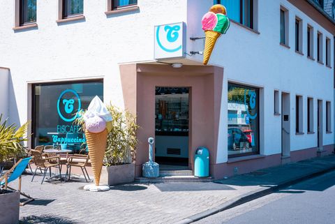 Eine Eisdiele mit einem einladenden Eingang und großen Eiskegel-Dekorationen. Die Fassade ist hell und freundlich, ideal für heiße Sommertage.