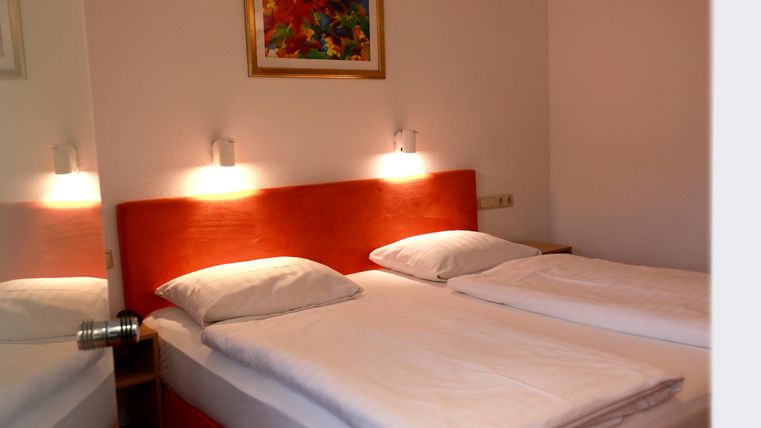 Ein gemütliches Schlafzimmer mit zwei Einzelbetten und modernen Wandleuchten. An der Wand hängt ein buntes Gemälde, das den Raum lebendig wirken lässt.