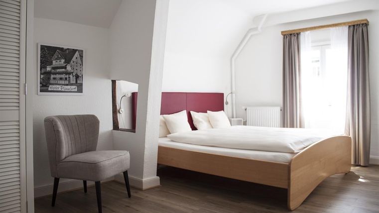 Ein modernes Schlafzimmer mit einem gemütlichen Bett und einer hellen Farbgestaltung. Ein bequemer Stuhl und ein Fenster mit Vorhängen runden den Raum ab.