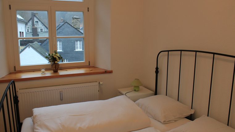Ein gemütliches Schlafzimmer mit einem schwarzen Bett und weißen Bettwäsche. Durch das Fenster ist ein Blick auf andere Häuser und die Landschaft sichtbar.